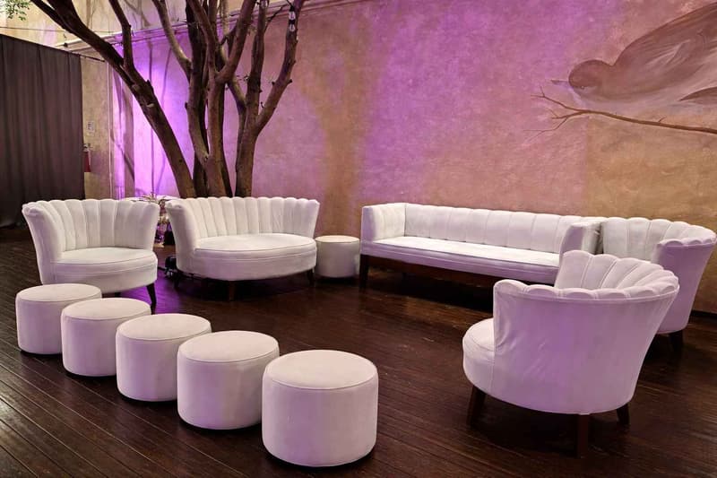Montaje de sala lounge con mobiliario tapizado en tonos claros, disposición semicircular para interacción social y ambientación con iluminación decorativa en espacio interior/exterior cubierto