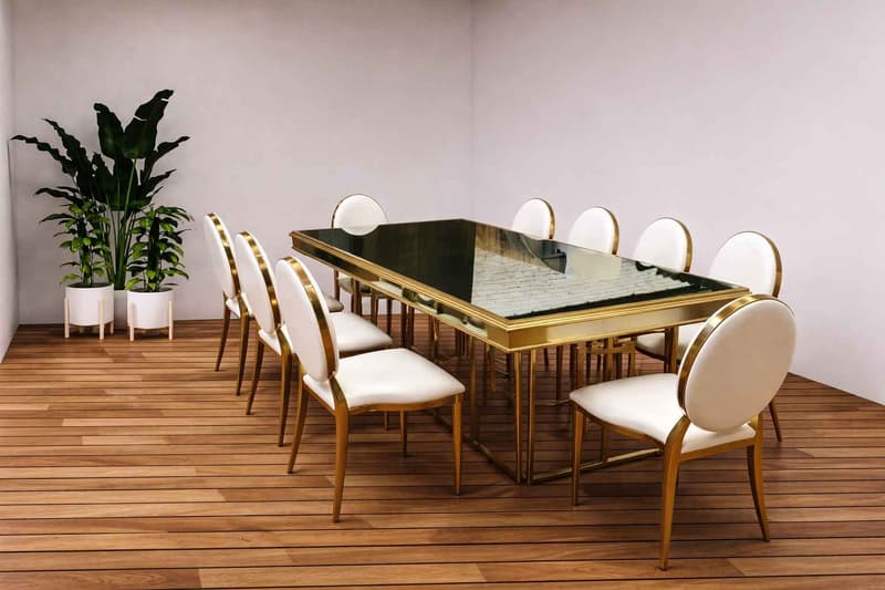 Montaje de comedor interior estilo moderno con mesa rectangular de cristal y estructura metálica dorada, acompañado de sillas tapizadas en tonos claros para eventos formales o reuniones ejecutivas