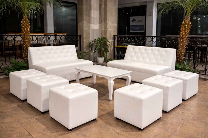 Montaje de sala lounge modular en tonos blancos con sofás, puffs y mesa central en entorno semi-exterior, ideal para áreas de descanso y networking en eventos sociales o corporativos